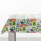 Christmas Wishes Kiwi Christmas Table Cloth draped over a table, featuring a colourful patchwork-style print with Christmas trees, native birds, wreaths, ornaments and festive details.