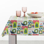 Christmas Wishes Kiwi Christmas Table Cloth styled on a dining table with pink glassware and a bowl of apples, showcasing the colourful festive print.