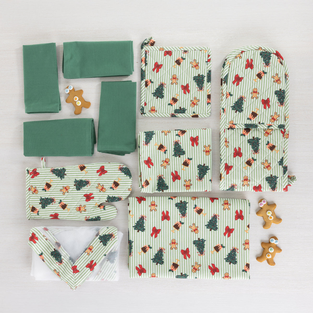 Christmas Wishes Classic Christmas kitchen collection arranged flat with green napkins, pot holders, oven gloves and food cover alongside gingerbread decorations.