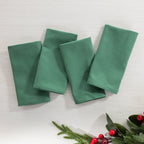 Christmas Wishes Classic Christmas 4 Pack Napkins arranged flat in a solid deep green colour with festive greenery and red berries styled nearby.