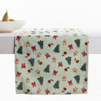 Christmas Wishes Classic Christmas Runner styled across a dining table, featuring green and white stripes with Christmas trees, gingerbread people, red bows and festive puddings.
