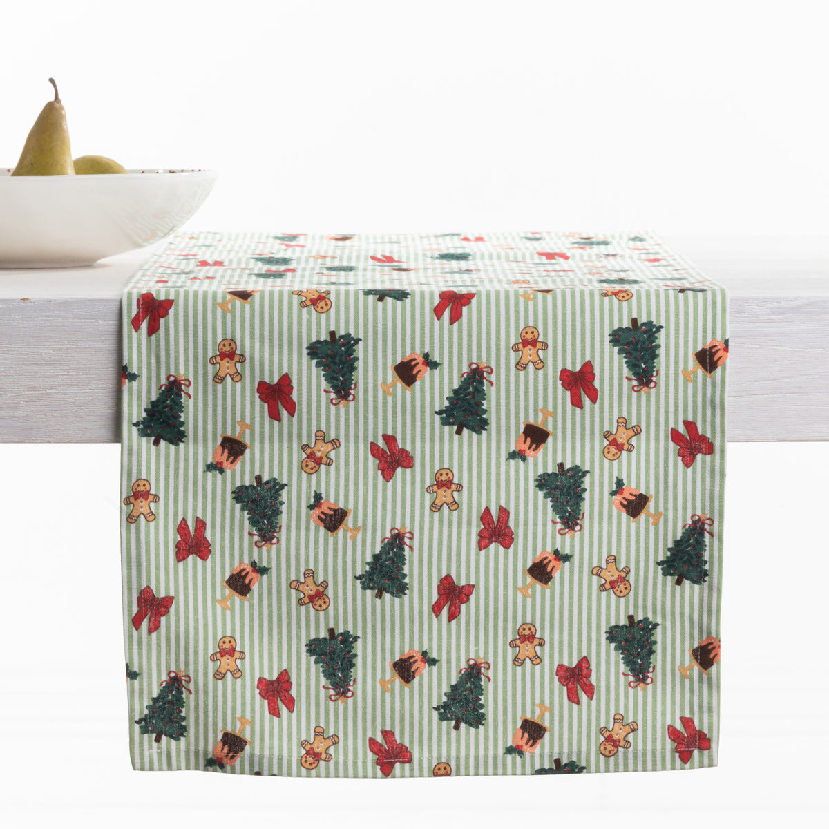 Christmas Wishes Classic Christmas Runner styled across a dining table, featuring green and white stripes with Christmas trees, gingerbread people, red bows and festive puddings.