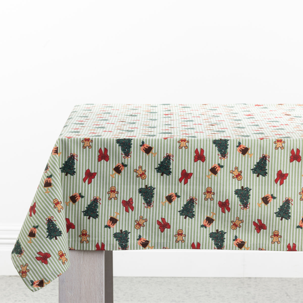 Christmas Wishes Classic Christmas Tablecloth draped over a dining table, featuring green and white stripes with Christmas trees, gingerbread people, red bows and festive puddings.