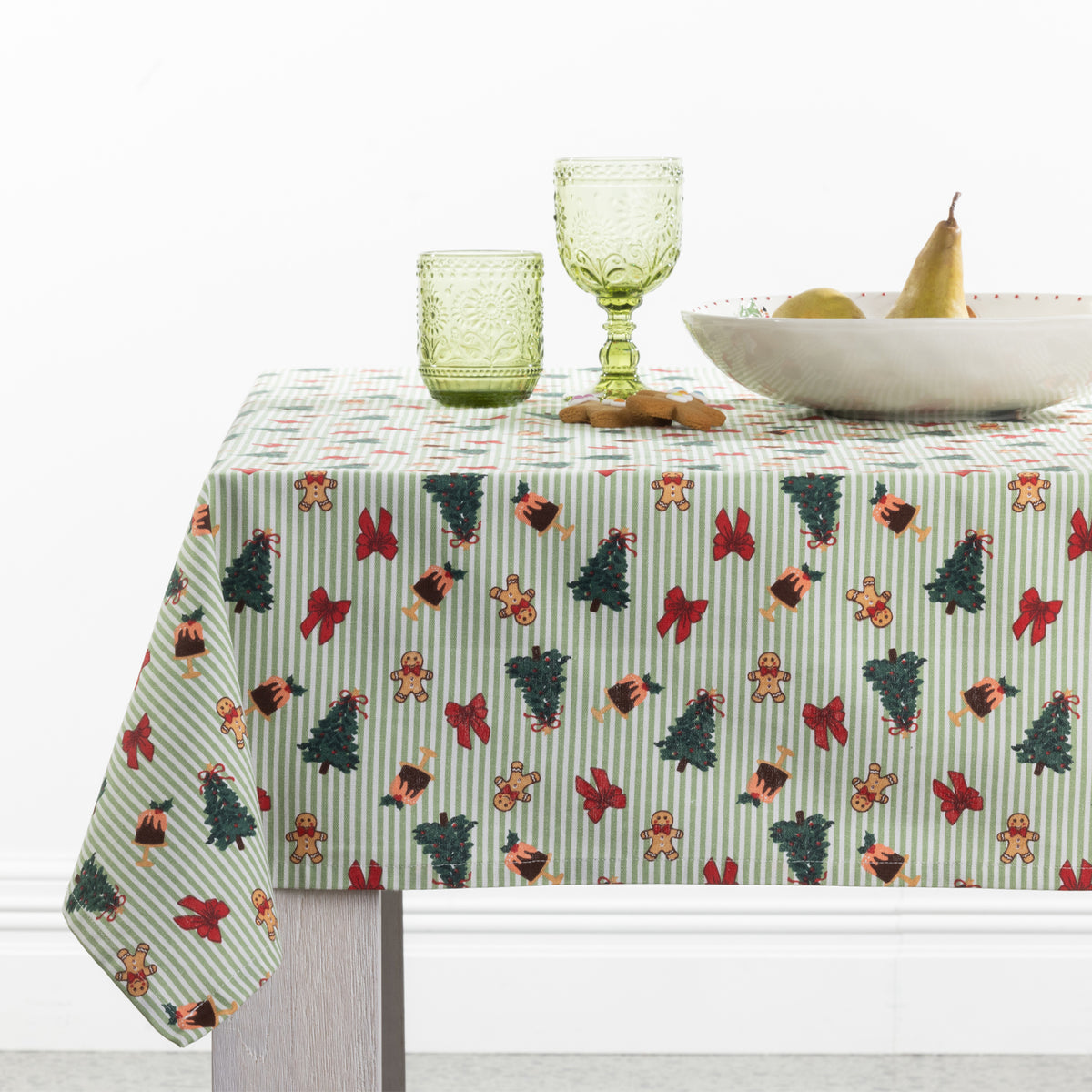 Christmas Wishes Classic Christmas Tablecloth styled on a dining table with green glassware, a white serving bowl and festive gingerbread decorations.