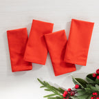 Christmas Wishes 4 Pack Napkins in solid red, arranged flat with festive greenery and red berries.