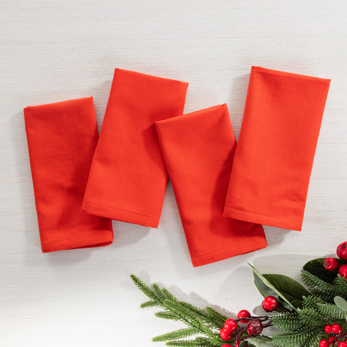 Christmas Wishes 4 Pack Napkins in solid red, arranged flat with festive greenery and red berries.