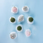 Assorted pink, green and champagne Christmas baubles featuring glitter, ribbed and decorative patterns, arranged on a snowy blue background.