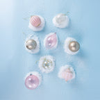 Assorted pink, white and champagne Christmas baubles featuring swirling glass designs, glitter accents and decorative patterns, arranged on a snowy blue background.