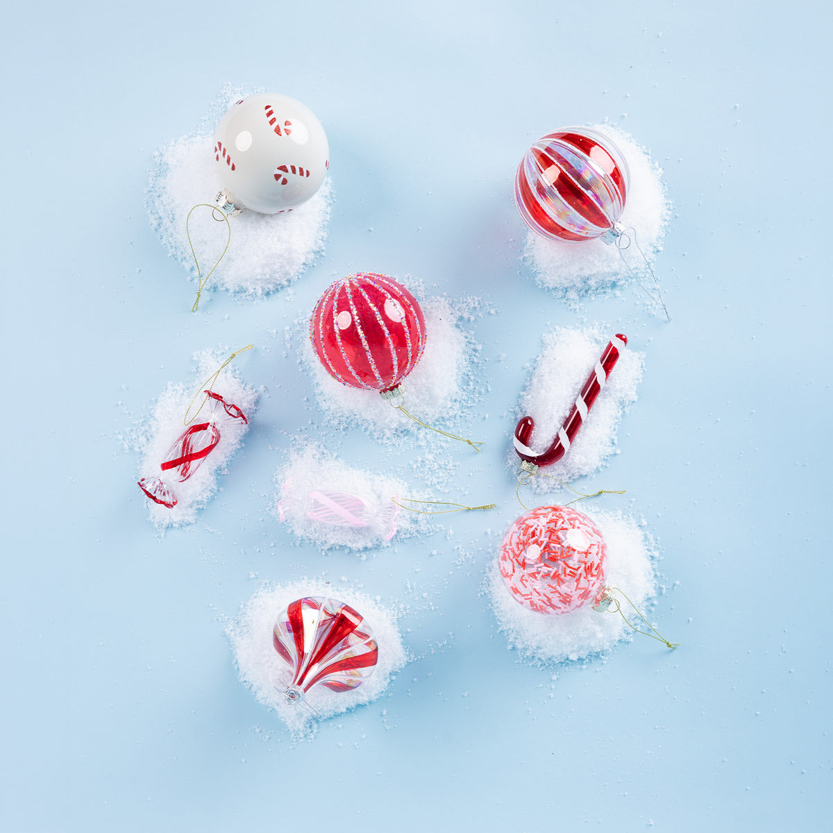 Assorted red, pink and white glass Christmas decorations featuring candy cane designs, glitter stripes and peppermint-inspired patterns, arranged on a snowy blue background.