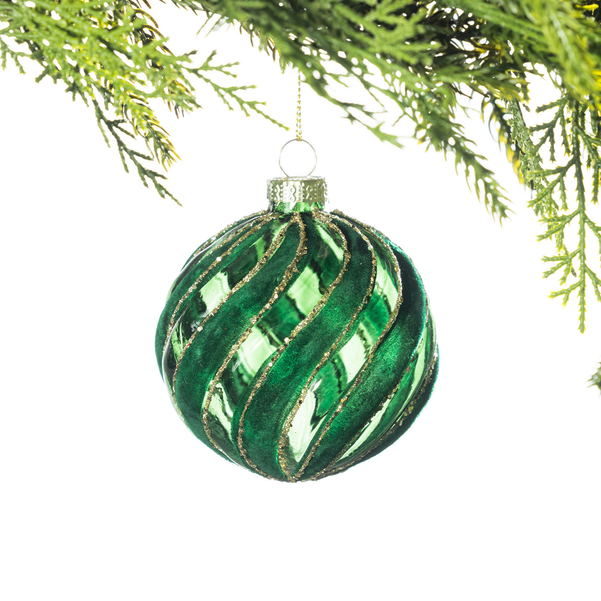 Green glass Christmas bauble featuring a swirling velvet design with gold glitter detailing, hanging from festive greenery against a white background.