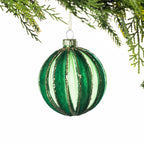 Green glass Christmas bauble featuring vertical velvet stripes with gold glitter detailing, hanging from festive greenery against a white background.
