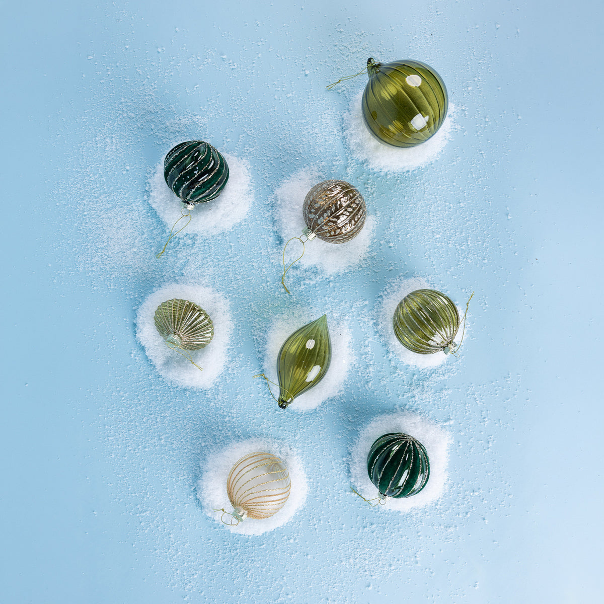 Green glass Christmas bauble featuring a swirling velvet design with gold glitter detailing, hanging from festive greenery against a white background.