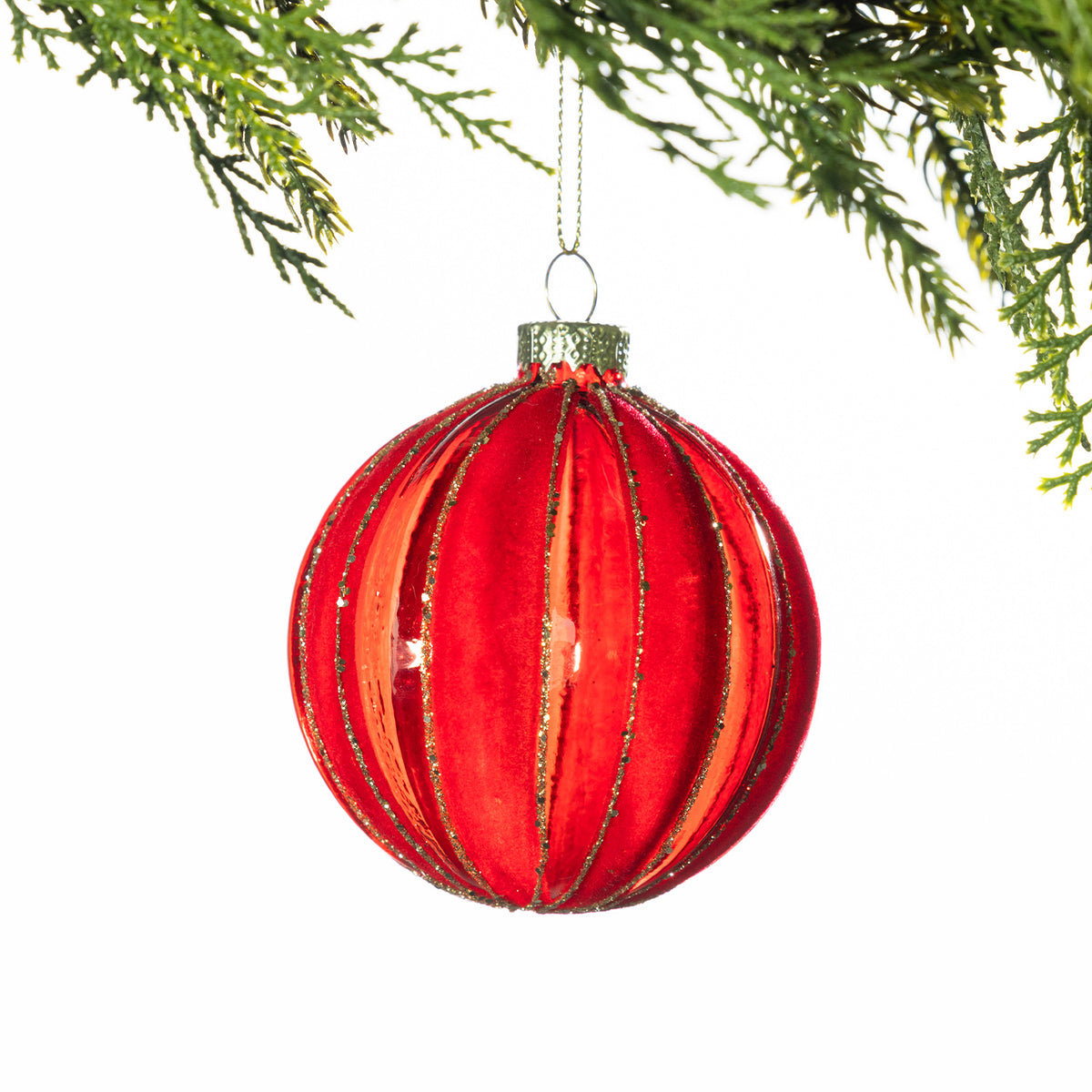 Red glass Christmas bauble featuring vertical velvet stripes with gold glitter detailing, hanging from festive greenery against a white background.