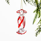 Clear glass Christmas lollie hanging decoration featuring bright red spiral stripes and red edging, hanging from festive greenery against a white background.