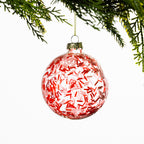 Clear glass Christmas bauble filled with red and pink sprinkles, hanging from festive greenery against a white background.