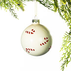 Cream glass Christmas bauble featuring red glitter candy cane patterns, hanging from festive greenery against a white background.
