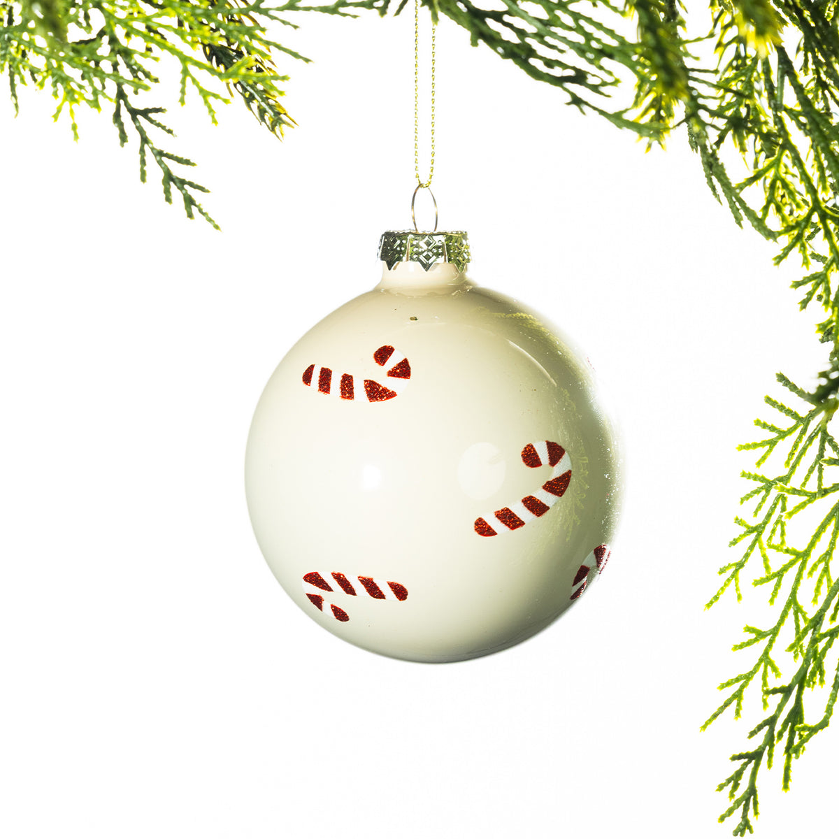 Cream glass Christmas bauble featuring red glitter candy cane patterns, hanging from festive greenery against a white background.