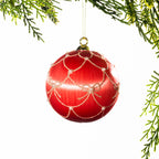 Light pink glass Christmas bauble featuring a red bow pattern and a large burgundy velvet bow, hanging from festive greenery against a white background.