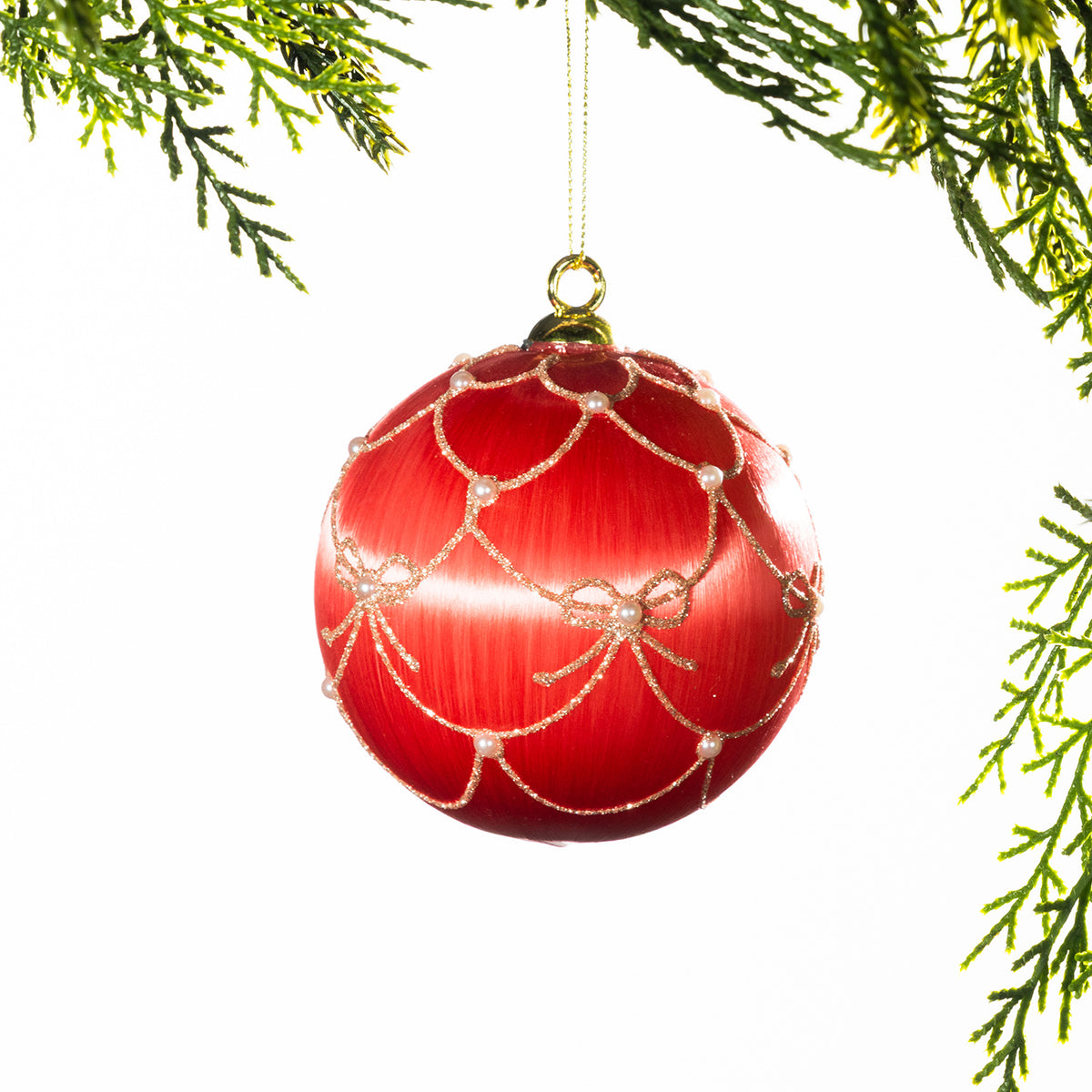 Light pink glass Christmas bauble featuring a red bow pattern and a large burgundy velvet bow, hanging from festive greenery against a white background.