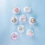 Assorted pink, silver and white Christmas baubles featuring glitter detailing and delicate patterns, arranged on faux snow against a light blue background.