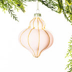 Light pink bell-shaped Christmas bauble featuring a soft velvet finish with gold glitter stripes, hanging from festive greenery against a white background.