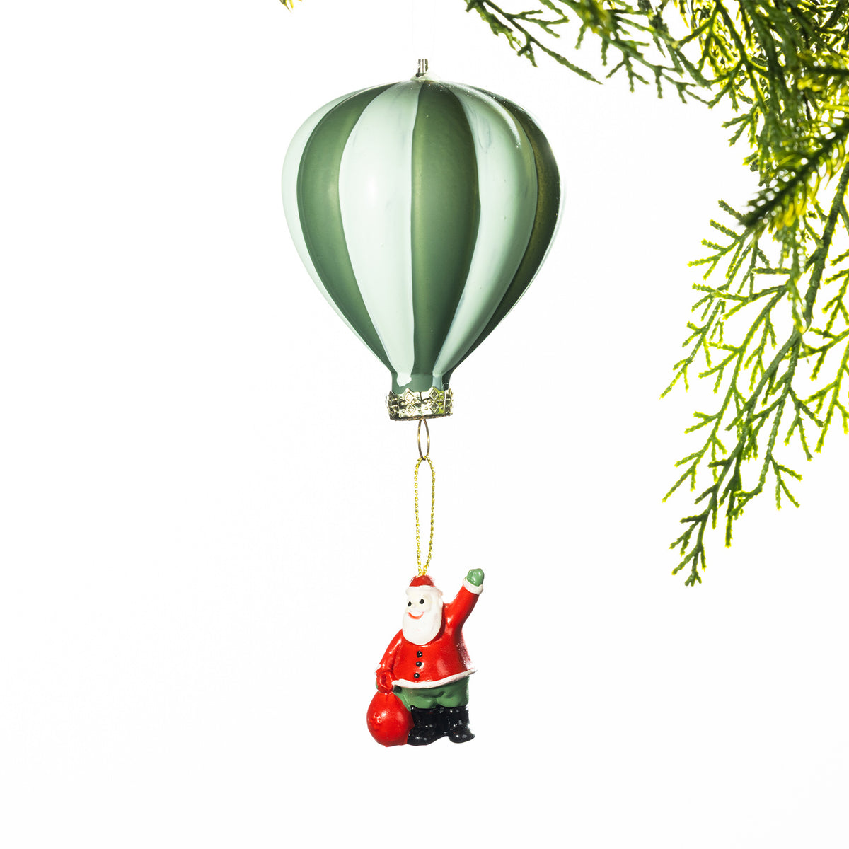 Green and white striped hot air balloon Christmas decoration with a miniature Santa holding a red sack suspended below, displayed against a white background with festive greenery.