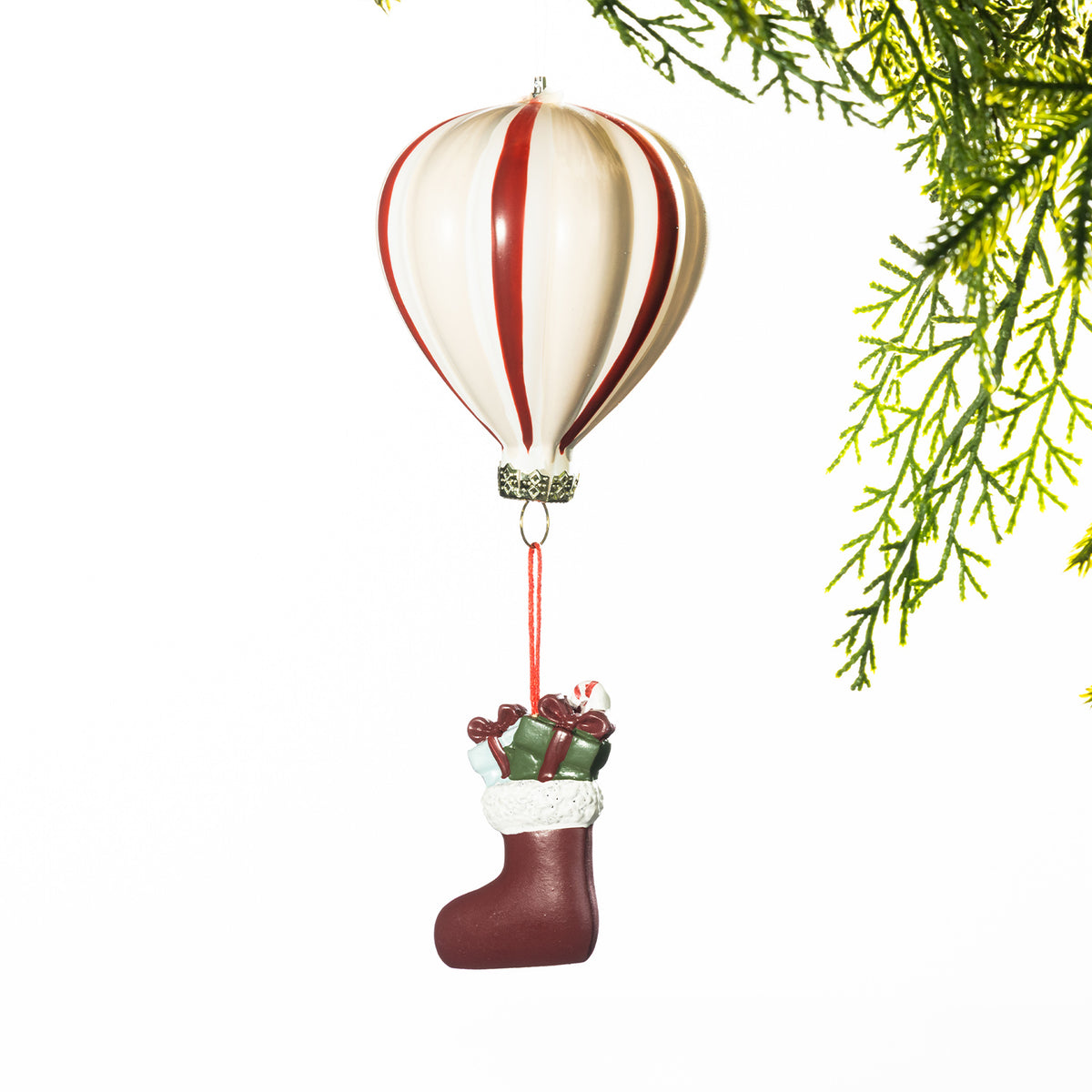 Cream and red striped hot air balloon Christmas decoration with a miniature stocking filled with presents suspended below, displayed against a white background with festive greenery.