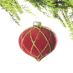 A red velvet onion-shaped Christmas bauble with a gold glitter lattice pattern hanging from festive greenery against a white background.