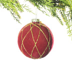 A round red velvet Christmas bauble featuring a gold glitter diamond lattice design hanging from festive greenery against a white background.