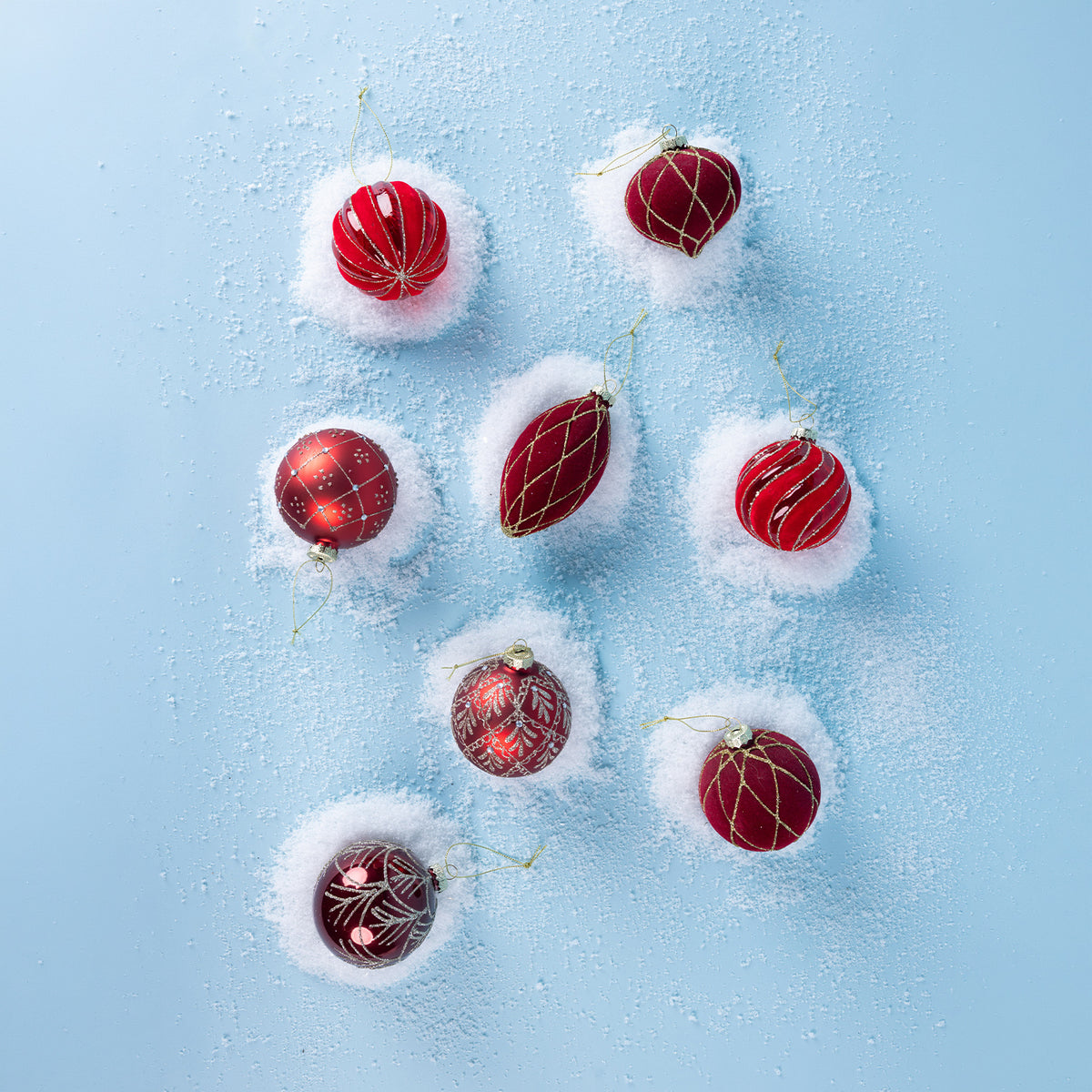 Assorted red and burgundy Christmas baubles with gold and silver glitter patterns, arranged on a snowy light blue background.