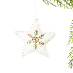 A white embroidered star hanging decoration featuring a green snowflake design with red accents and red stitching around the edges, suspended from festive greenery against a white background.