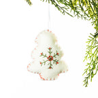 A white embroidered Christmas tree hanging decoration featuring a green snowflake design with red accents and red stitching around the edges, suspended from festive greenery against a white background.