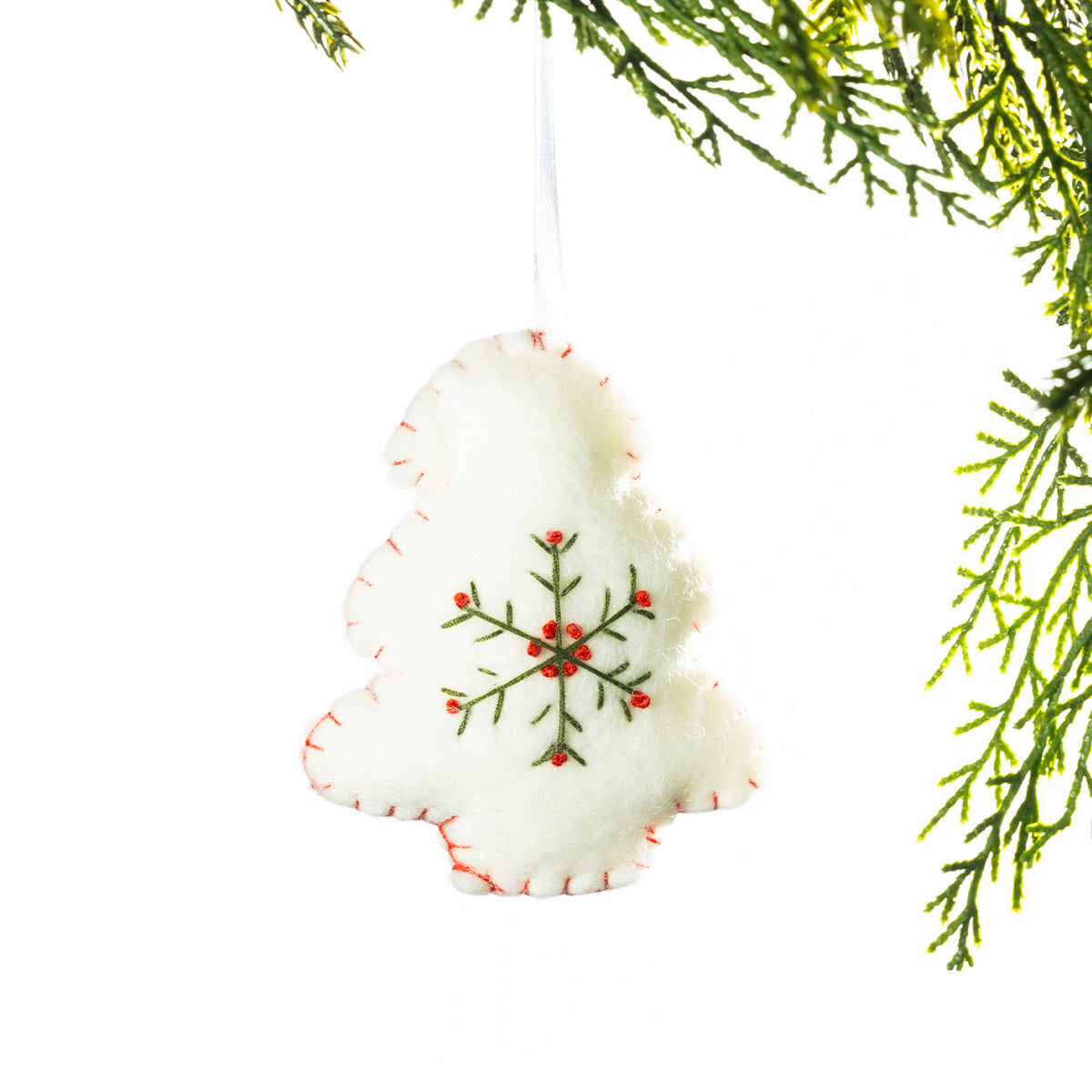A white embroidered Christmas tree hanging decoration featuring a green snowflake design with red accents and red stitching around the edges, suspended from festive greenery against a white background.