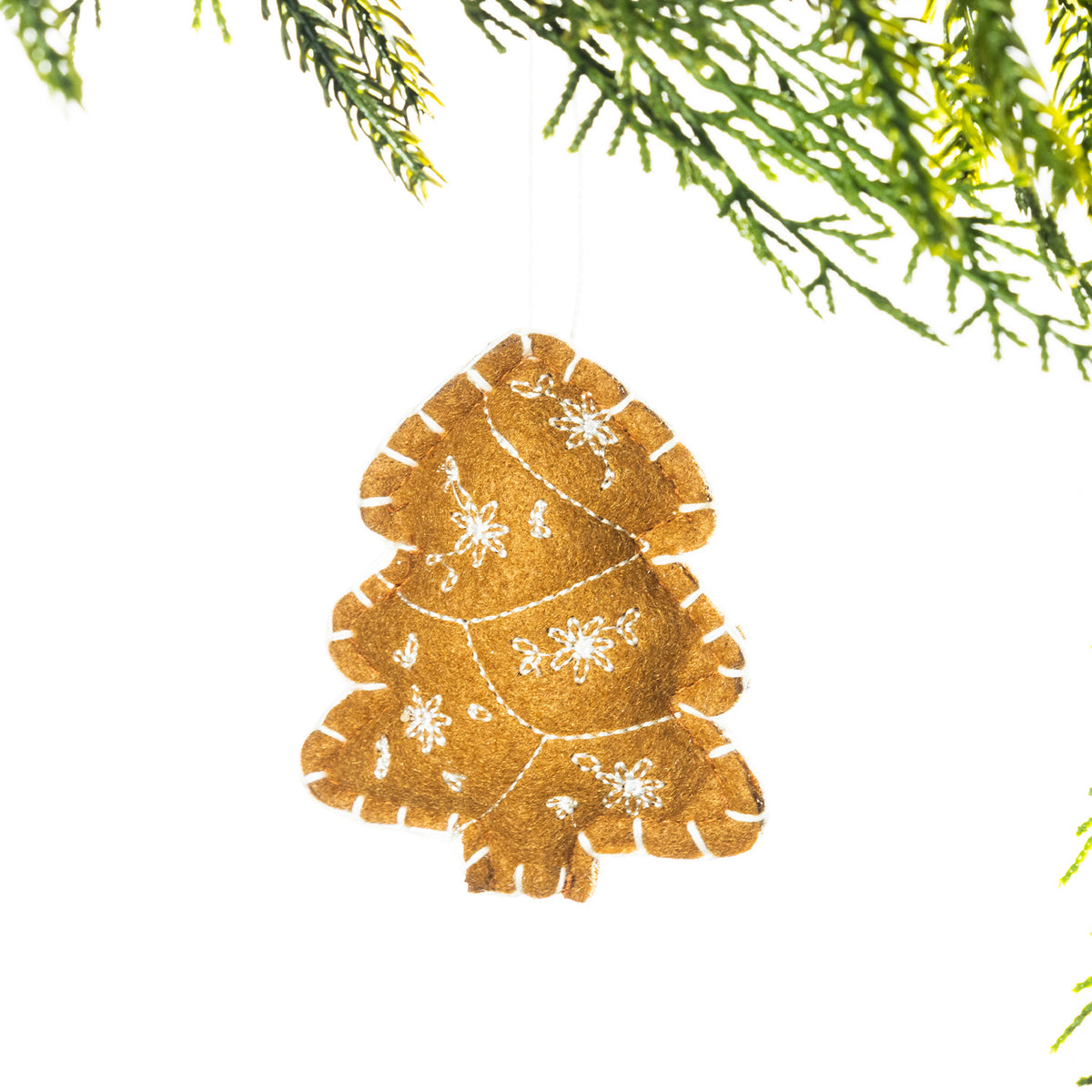 A gingerbread-coloured embroidered Christmas tree hanging decoration featuring white snowflake stitching, suspended from festive greenery against a white background.