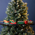A miniature Christmas train set on a black track, featuring Santa in a red sleigh, a green passenger car, and a red and gold locomotive, displayed against a dark blue background with a flocked Christmas tree.