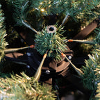 Close-up of a black metal train support rods latched onto Christmas tree trunk.