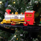 A toy model locomotive train with a red caboose, silver boiler, and gold details, displayed on a black track against a blurred Christmas tree background with warm lights.