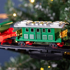 A green toy train passenger car with red and gold details, mounted on a black track, photographed against a blurred Christmas tree background with warm lights.