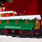 A green Christmas-themed train car with 'Merry Christmas' written on the side, featuring white snow-dusted roofs, gold accents, and red wheels, photographed on a snowy surface with a blurred festive background.