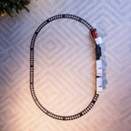 A train set with a black track laid in a large loop on a textured light beige surface, with a red and white Christmas-themed train pulling several white passenger cars.