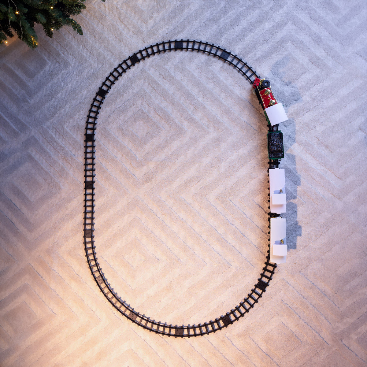 A train set with a black track laid in a large loop on a textured light beige surface, with a red and white Christmas-themed train pulling several white passenger cars.