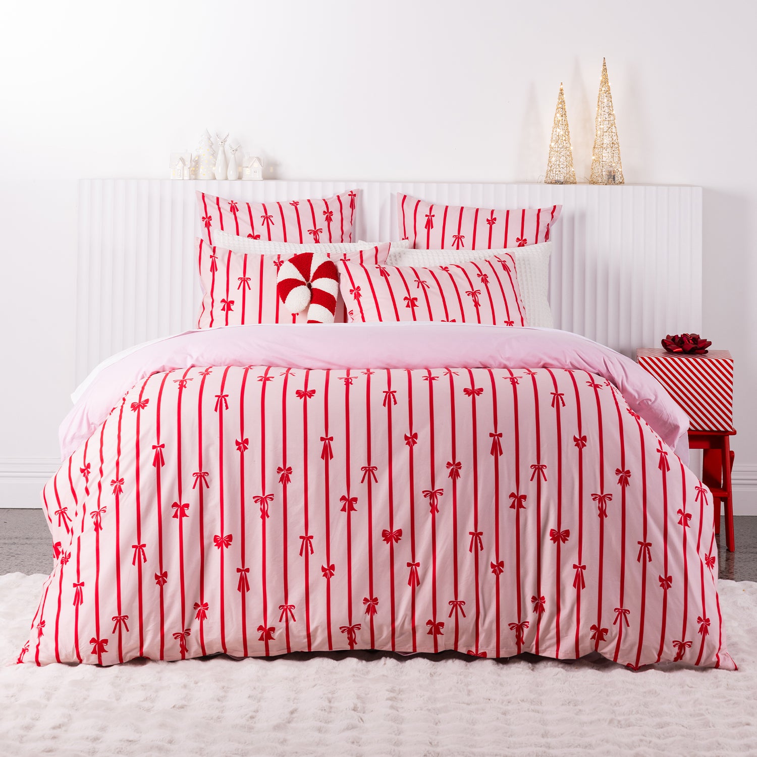 Christmas Wishes Bows Duvet Cover Set featuring a festive red bow and stripe pattern on a soft pink background, styled in a Christmas-themed bedroom.