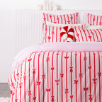 Close-up of the Christmas Wishes Bows Duvet Cover Set, showcasing the red bow and stripe design with a plain pink reverse and matching pillowcases.