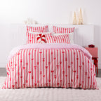 Christmas Wishes Bows Duvet Cover Set featuring a festive red bow and stripe pattern on a soft pink background, styled in a Christmas-themed bedroom.