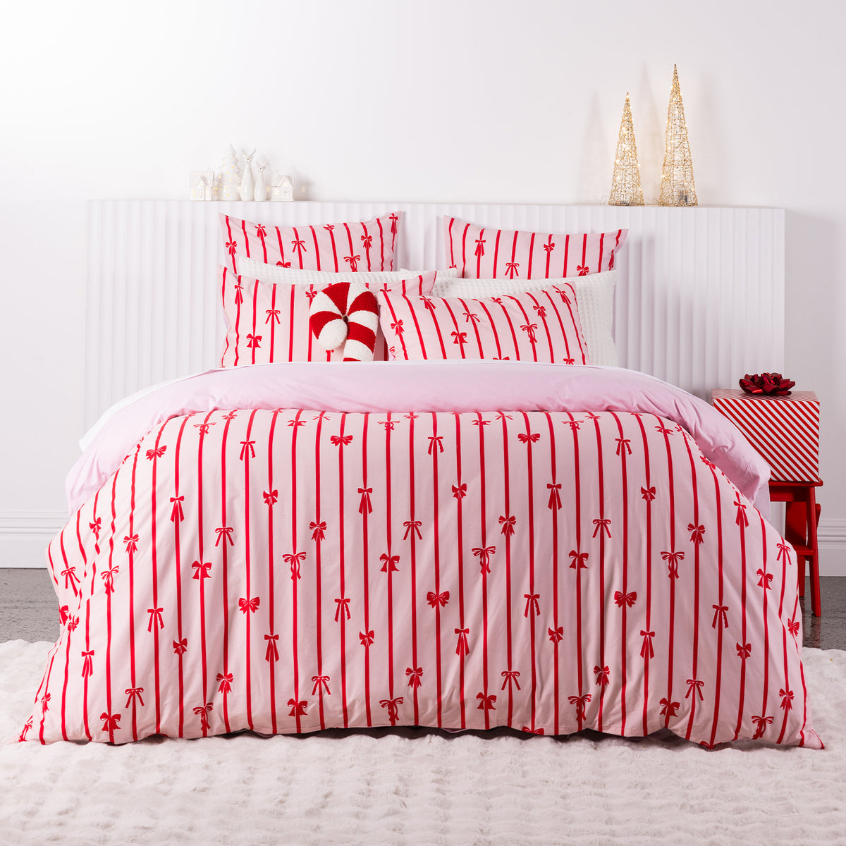 Christmas Wishes Bows Duvet Cover Set featuring a festive red bow and stripe pattern on a soft pink background, styled in a Christmas-themed bedroom.