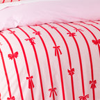 Christmas Wishes Bows Duvet Cover Set in Pink and Red, styled with matching pillowcases, white textured cushions and a red and white candy cane cushion.