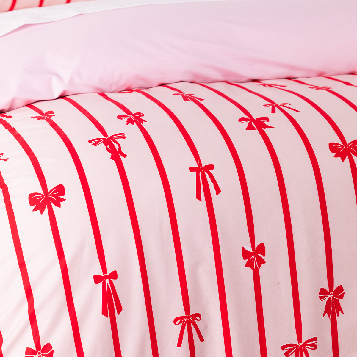 Christmas Wishes Bows Duvet Cover Set in Pink and Red, styled with matching pillowcases, white textured cushions and a red and white candy cane cushion.
