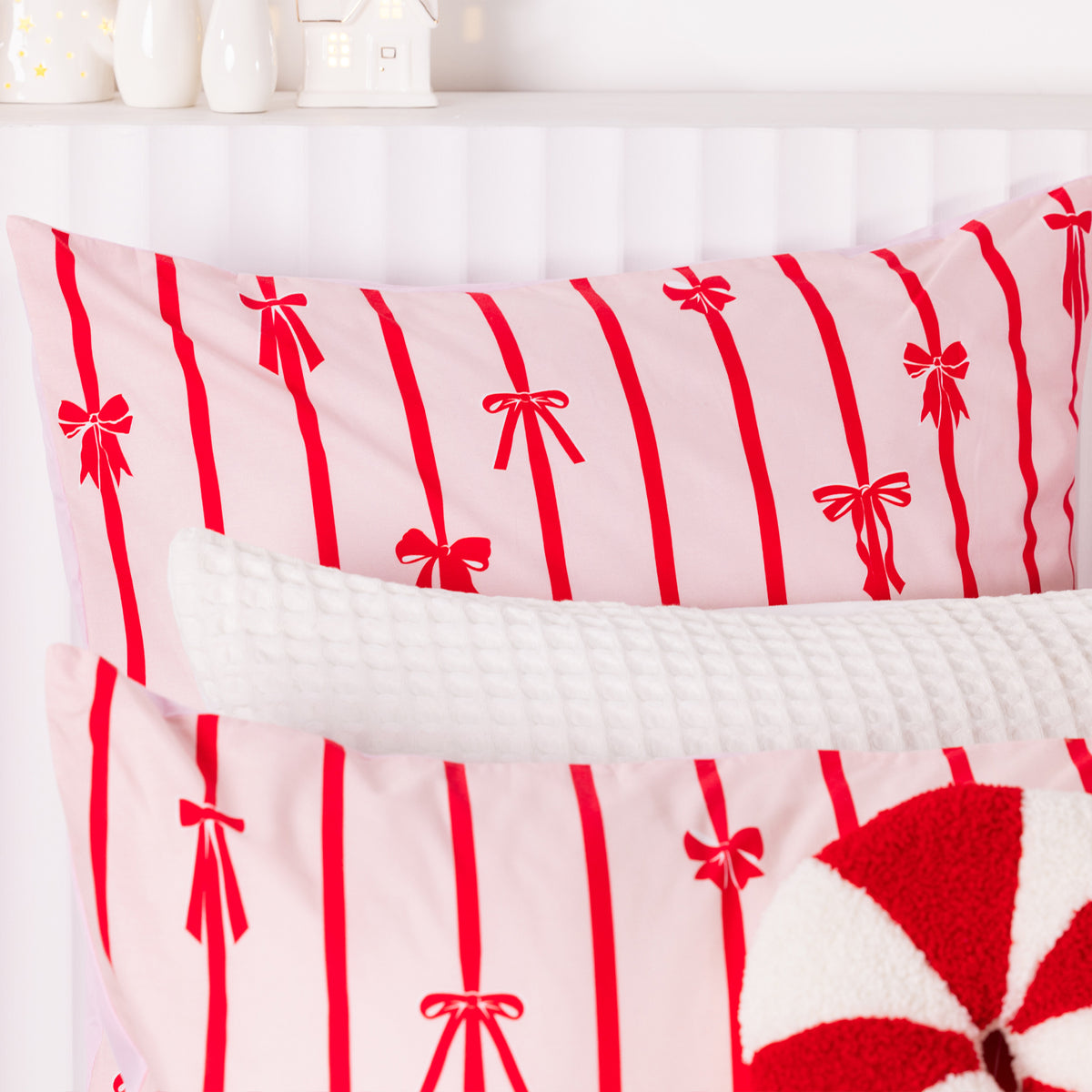 Close-up of the Christmas Wishes Bows Euro Pillowcase featuring red stripes and bows on a soft pink background.