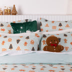 Close-up of the matching Sugar Spruce pillowcases styled with a green festive cushion, white textured pillows and a gingerbread man cushion.