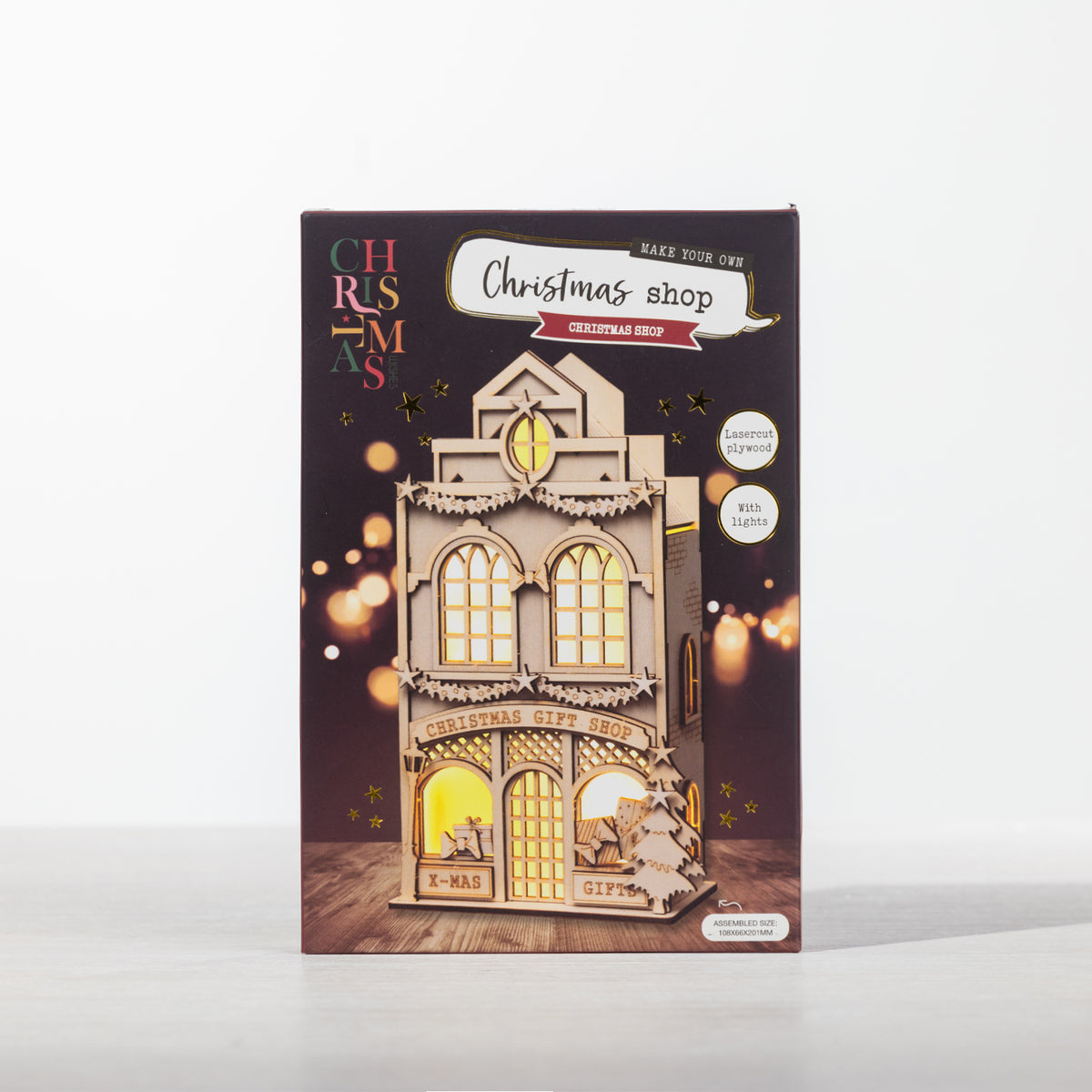 Make Your Own Christmas Shop puzzle kit presented in its festive packaging, featuring a detailed laser-cut plywood shop design with built-in lights.
